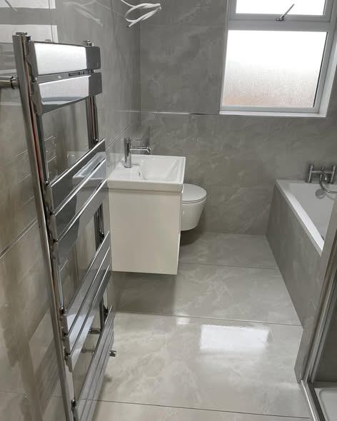 Grey marble-effect bathroom with a bath, wall-hung toilet, vanity and chrome towel rail