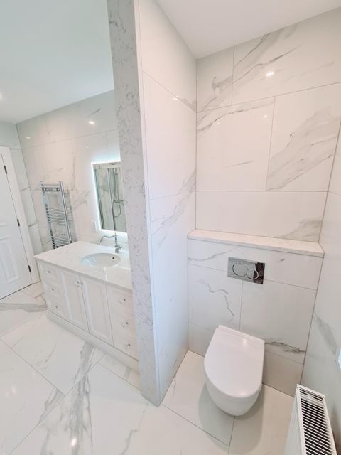 Marble-effect bathroom with a stone-topped vanity, backlit mirror and wall-hung toilet
