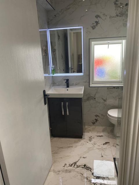 En-suite with bold marble-effect tiles, dark vanity unit and backlit mirror