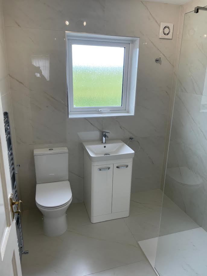 After: the same bathroom with a walk-in shower, white vanity unit, new toilet and large marble-effect tiles