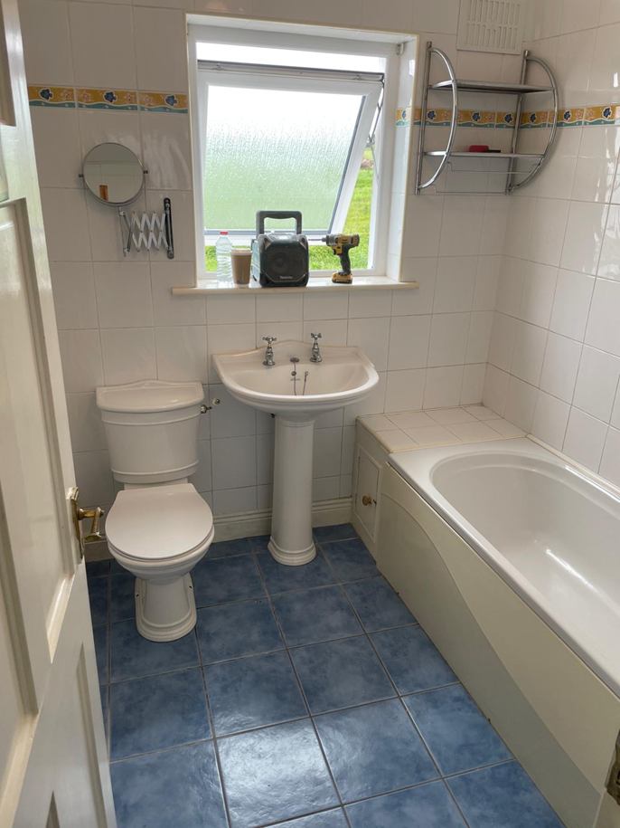 Before: bathroom with a white bath, pedestal sink, patterned border tiles and blue floor tiles